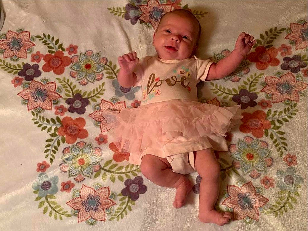 Serenity is registered to the contest to win money with this photo: baby, baby_products, baby_toddler_clothing, child, comfort, embellishment, face, happy, linens, magenta, pattern, peach, person, pink, room, sitting, skin, sleeve, smile, textile
