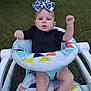 baby, child, infant, bow, headband, black_shirt, baby_seat, colorful_pattern, grass, outdoor, legs, arms, fists, determined_expression, fisher_price, person, cute, young, sitting, playful