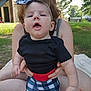 Winifred is registered to the contest to win money with this photo: baby, child, person, headband, bow, black_shirt, checkered_pants, outdoor, grass, blanket, adult, hands, face, expression, nature, sunlight, building, summer, casual, sitting
