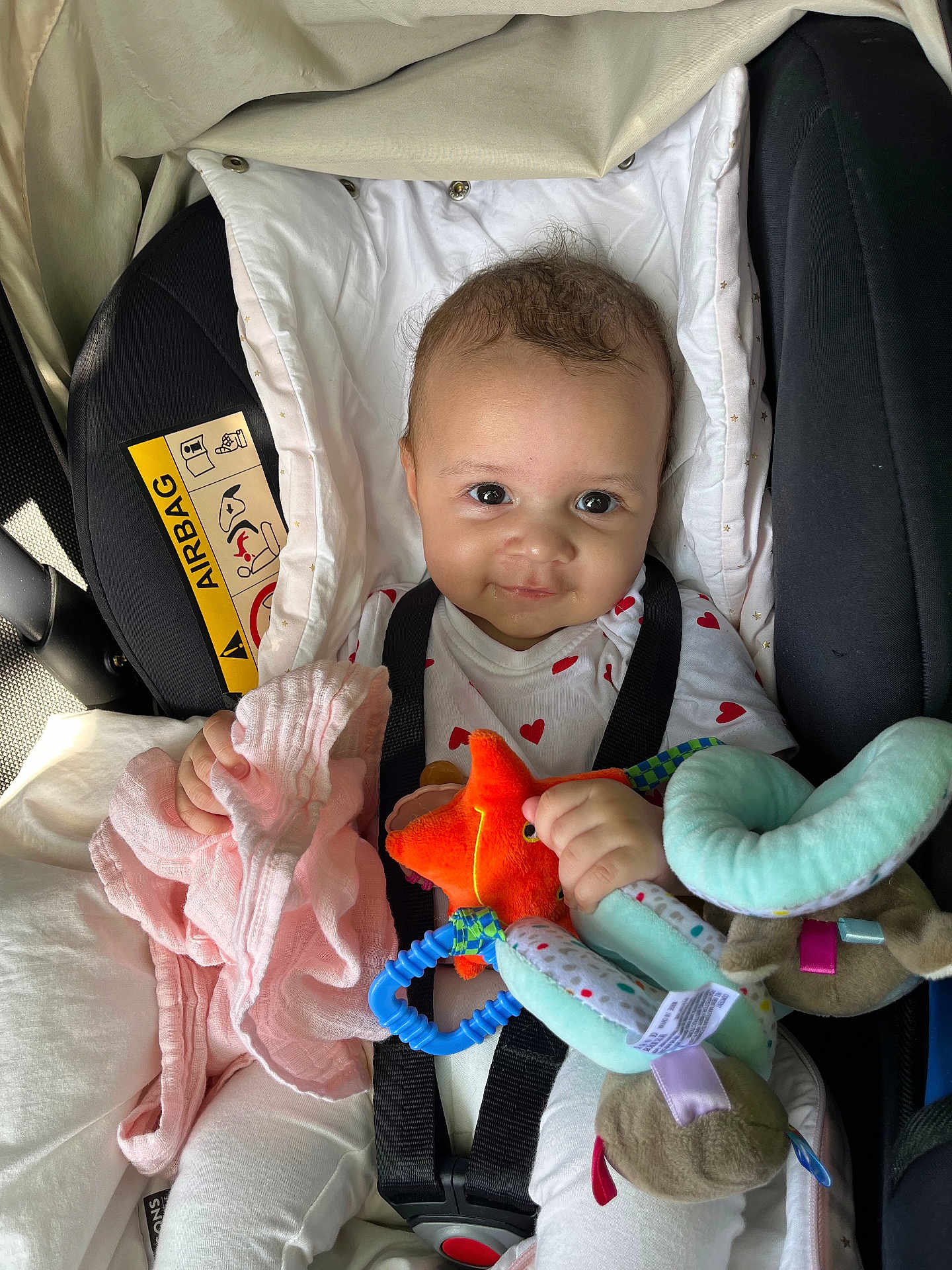 Mallory participe au concours pour gagner de l'argent avec cette photo : baby, car_seat, child, plush_toy, soft_toy, pink_cloth, smile, infant, seatbelt, white_clothing, heart_pattern, indoor, cute, happy, face, human, child_safety, car_interior, toy, comfort