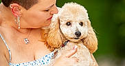 Arya is registered to the contest to win money with this photo: woman, dog, poodle, pet, tattoo, ear_piercing, jewelry, necklace, bracelet, short_hair, fluffy_dog, holding, outdoor, green_background, portrait, love, affection, closeup, summer_dress, nature