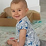 baby, child, smiling, sitting, indoor, cute, happy, cartoon_print, short_hair, face, toys, floor, clothing, skin, person, young_child, playful, background_blur, room, expression