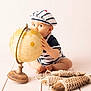 baby, child, globe, striped_clothing, beret, wooden_floor, wooden_fish, decorations, starfish, nautical, curious, sitting, indoors, soft_lighting, vintage, playful, cute, portrait, floor, toy