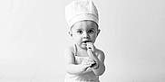 Lucas a rejoint le concours — aidez-le/la à gagner de superbes lots ! baby, chef_hat, apron, wooden_spoon, glass_jar, sitting, curious, monochrome, black_and_white, infant, cute, studio, portrait, child, kitchen, cooking, food, expression, smiling, playful