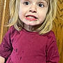 child, girl, blonde_hair, face, expression, teeth, dress, burgundy_clothing, messy_hair, indoor, wooden_door, curious, funny_face, young_child, casual_clothing, portrait, person, stain, messy, closeup