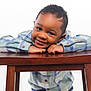 Tymair is registered to the contest to win money with this photo: child, smiling, plaid_shirt, wooden_table, happy, portrait, cute, young_boy, casual_clothing, indoor, person, face, eyes, hands, studio_lighting, short_hair, buttoned_shirt, leaning, friendly, background