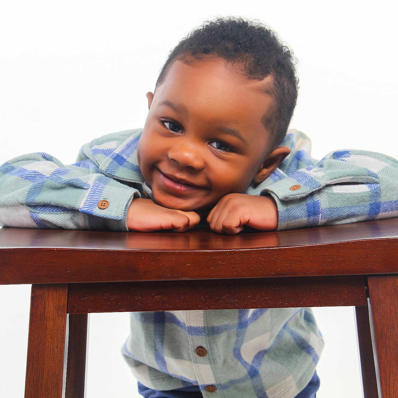 Tymair is registered to the contest to win money with this photo: background, buttoned_shirt, casual_clothing, child, cute, eyes, face, friendly, hands, happy, indoor, leaning, person, plaid_shirt, portrait, short_hair, smiling, studio_lighting, wooden_table, young_boy