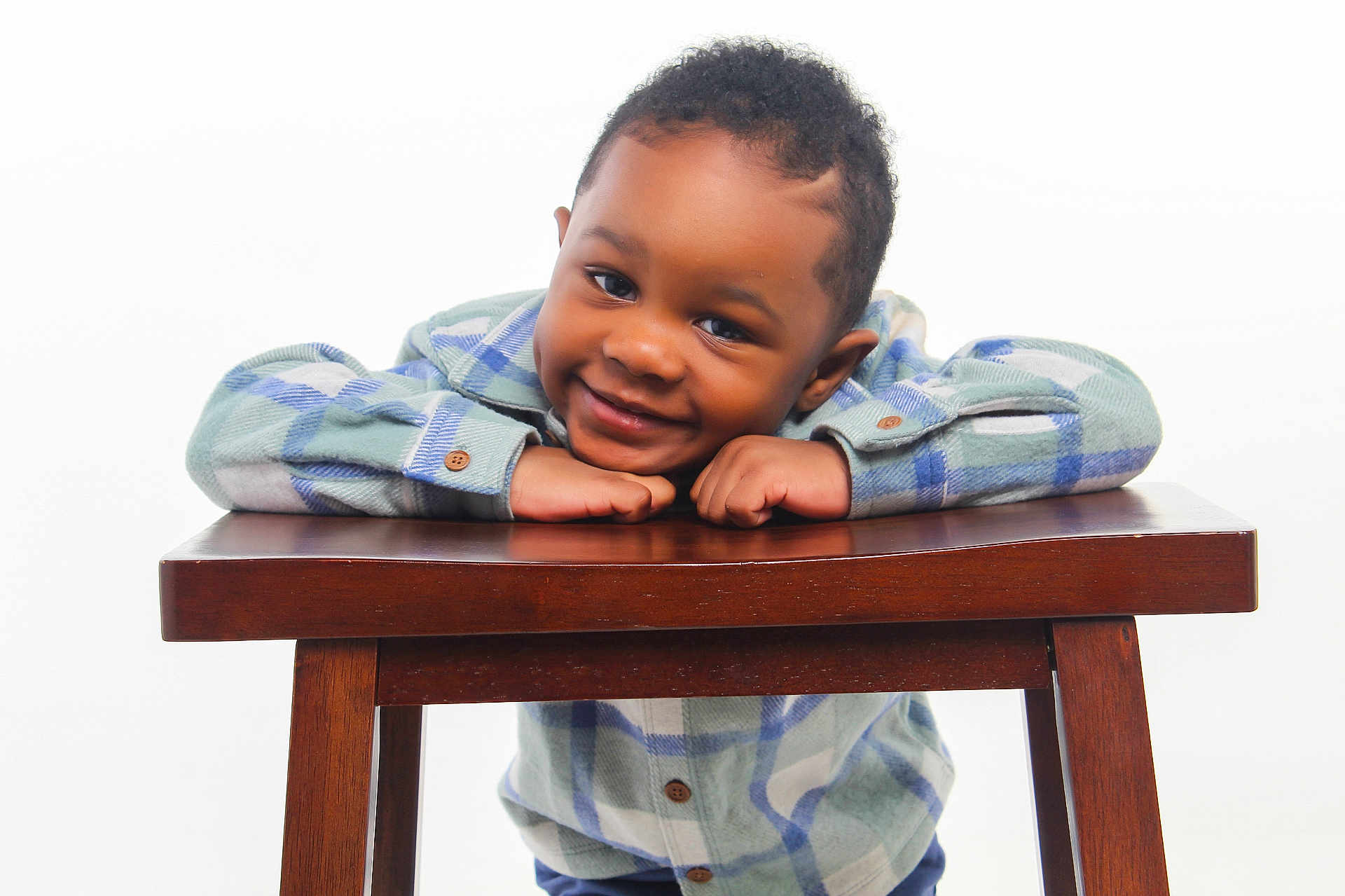 Tymair is registered to the contest to win money with this photo: child, smiling, plaid_shirt, wooden_table, happy, portrait, cute, young_boy, casual_clothing, indoor, person, face, eyes, hands, studio_lighting, short_hair, buttoned_shirt, leaning, friendly, background