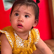 Làanh a rejoint le concours — aidez-le/la à gagner de superbes lots ! baby, child, clothing, curious, cute, expression, eyes, face, hair_buns, indoors, person, portrait, red_background, sitting, skin, small_shoes, toddler, wooden_floor, yellow_dress, young_child