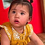baby, child, clothing, curious, cute, expression, eyes, face, hair_buns, indoors, person, portrait, red_background, sitting, skin, small_shoes, toddler, wooden_floor, yellow_dress, young_child