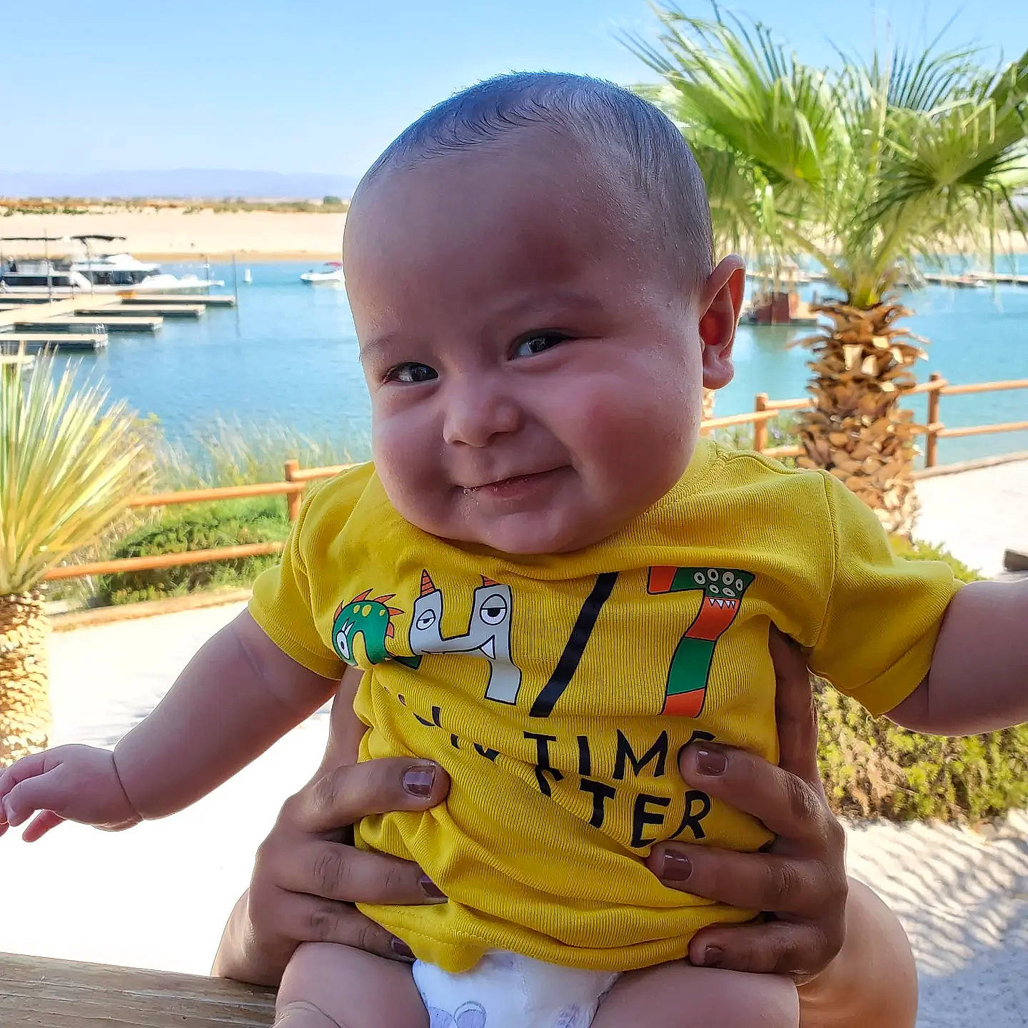 Azriel is registered to the contest to win money with this photo: azure, baby_toddler_clothing, chin, eye, face, finger, gesture, hand, happy, head, iris, nose, person, plant, skin, sky, sleeve, smile, thumb, water