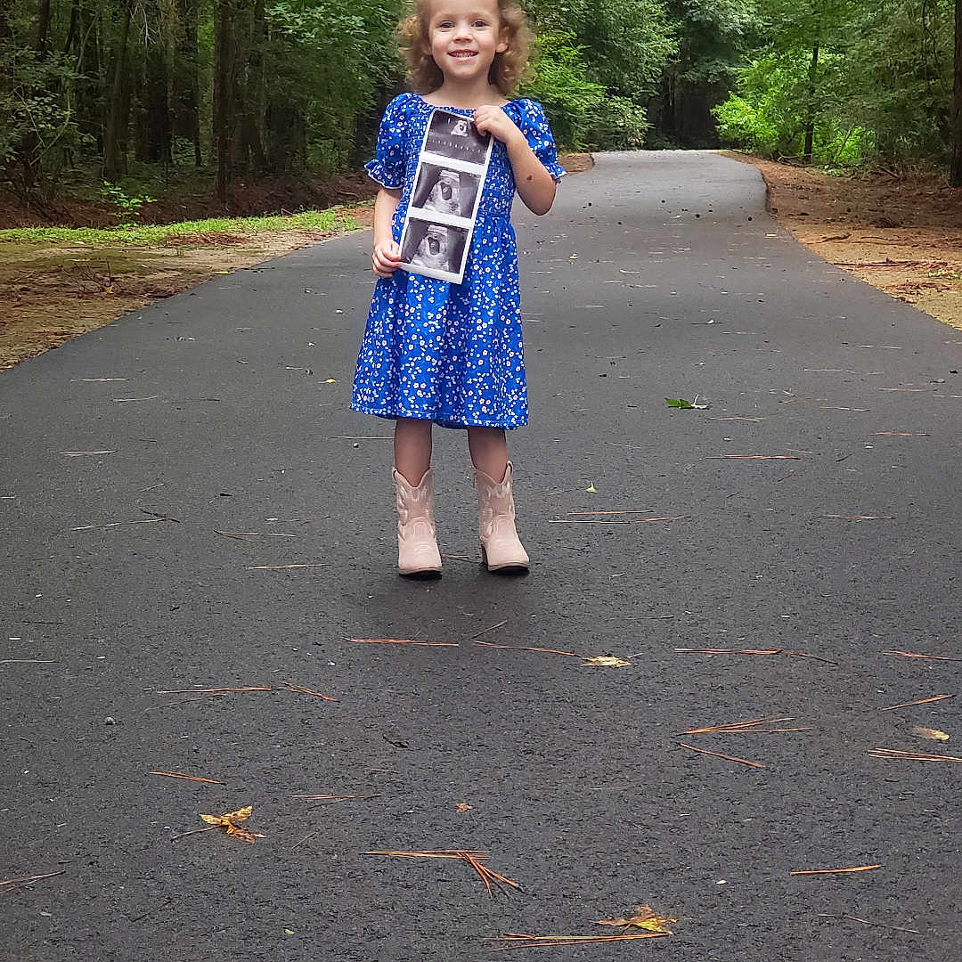 Fraust is registered to the contest to win money with this photo: child, clothing, dress, face, female, footwear, girl, head, pants, person, photography, plant, portrait, road, shoe, shorts, tarmac, tree, vegetation, walking