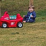 Morrison joined the competition — help win amazing prizes! child, toddler, grass, toy_truck, outdoor, barefoot, pacifier, blue_clothing, red_toy, playing, smiling, wooden_post, nature, daylight, greenery, happy, sitting, young_child, casual, fun