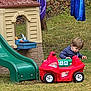 Morrison is registered to the contest to win money with this photo: toddler, child, toy_car, playhouse, slide, grass, outdoor, backyard, blue_fabric, autumn_leaves, curious, playing, plastic_toy, green_slide, red_car, young_child, casual_clothing, daylight, nature, fun