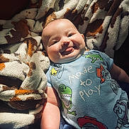 Kolsen is registered to the contest to win money with this photo: baby, infant, tongue_out, onesie, cartoon_characters, blanket, patterned_blanket, soft_texture, smiling, chubby_cheeks, cute, lying_down, playful, indoors, child, happy, portrait, light_and_shadow, cozy, person