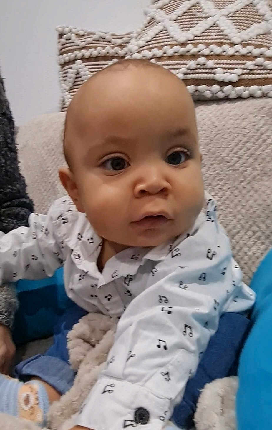 Oscar a rejoint le concours — aidez-le/la à gagner de superbes lots ! baby, child, indoor, couch, pillow, clothing, shirt, music_notes, face, person, sitting, blanket, cozy, expression, cute, young_child, portrait, home, soft, curious