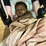 Milan joined the competition — help win amazing prizes! baby, blanket, brown_skin, car_seat, child, cozy, cushion, dark_hair, face, hands, indoor, infant, nursery, pacifier, portrait, rainbow_pattern, relaxed, seated, sleeping, wooden_floor