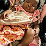 baby, blanket, bottle, car_seat, child, close_up, cozy, curly_hair, dark_skin, heart_pattern, indoors, infant, peaceful, pink_clothing, portrait, rainbow_pattern, resting, seated, sleeping, textile