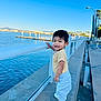 toddler, child, smiling, outdoor, waterfront, railing, blue_sky, casual_clothing, white_shoes, concrete, daylight, happy, person, nature, urban, sidewalk, park, leisure, young_child, standing