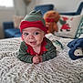 Benoît participe au concours pour gagner de l'argent avec cette photo : baby, child, infant, blanket, plush_toy, gingerbread_man, holiday, christmas, elf_costume, hat, face, tongue_out, smiling, indoor, couch, pillow, cozy, home, cute, playful