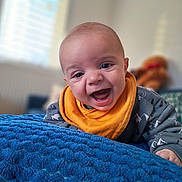 Benoît participe au concours pour gagner de l'argent avec cette photo : baby, smiling, orange_bib, blue_blanket, indoor, cozy, plush_toy, teddy_bear, happy, child, face, portrait, crawling, home, soft_light, cute, apparel, infant, blanket_texture, furniture