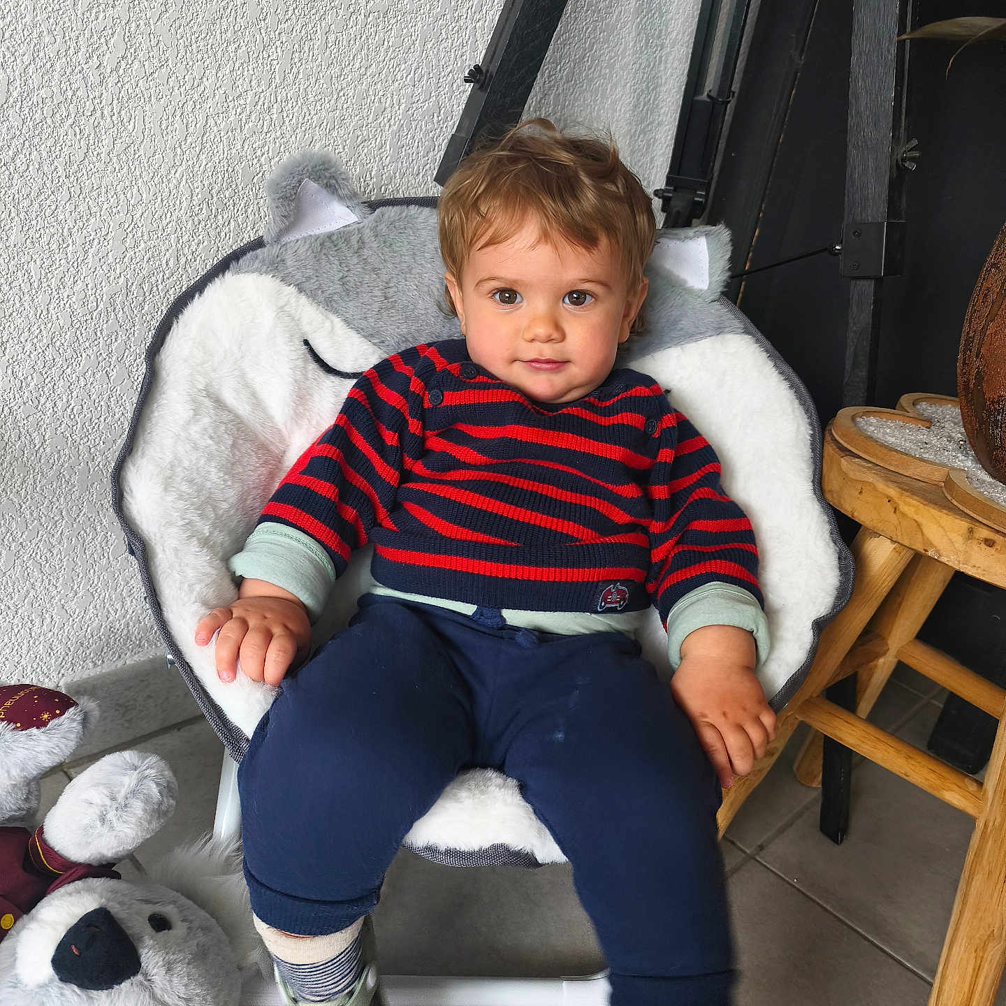 Lyano participe au concours pour gagner de l'argent avec cette photo : toddler, child, chair, plush_chair, striped_sweater, navy_pants, socks, shoes, plush_toy, koala_toy, wooden_stool, tile_floor, indoor, wall_texture, cute, smiling, seated, person, home_interior, furniture