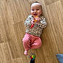 baby, child, clothing, cute, floor, foot, happy, holding, indoors, infant, keys, leopard_print, lying_down, person, pink_pants, playful, smiling, sock, toy, wooden_floor