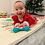 baby, background, carpet, child, christmas_tree, cute, decorations, face, festive, floor, hands, happy, holiday, indoors, person, play_mat, red_dress, smiling, toddler, toy