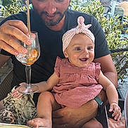 Alba participe au concours pour gagner de l'argent avec cette photo : baby, child, man, smile, happy, pink_dress, headband, glass, drink, straw, orange_slice, outdoor, restaurant, table, chair, plant, greenery, person, seated, casual