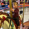 Raealyn is registered to the contest to win money with this photo: background, carousel, child, clothing, colorful, expression, fence, flooring, footwear, golden_pole, hair, horse, indoor, people, playful, ride, seat, seatbelt, shopping_mall, toddler