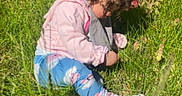Raealyn joined the competition — help win amazing prizes! casual_clothing, child, closeup, curly_hair, daylight, field, grass, greenery, leggings, nature, outdoor, person, pink_bow, pink_jacket, playing, sitting, sneakers, sunlight, toddler, young_child