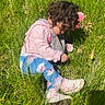 casual_clothing, child, closeup, curly_hair, daylight, field, grass, greenery, leggings, nature, outdoor, person, pink_bow, pink_jacket, playing, sitting, sneakers, sunlight, toddler, young_child