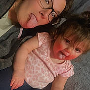 Raealyn is registered to the contest to win money with this photo: adult, baby, child, glasses, tongue, playful, smiling, casual_clothing, indoor, person, cute, fun, family, toddler, pink_shirt, dark_pants, lying_down, cozy, happy, portrait