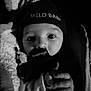 baby, black_and_white, close_up, hat, pacifier_clip, child, infant, warm_clothing, hand, face, portrait, cozy, newborn, cute, indoor, soft_light, knit_hat, expression, young_child, wrapped