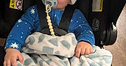 Princeton is registered to the contest to win money with this photo: baby, pacifier, hat, blanket, car_seat, blue_pajamas, child, indoor, cute, infant, sitting, warm_clothing, safety_harness, floor, wood_floor, soft_toy, comfort, portrait, expression, hand