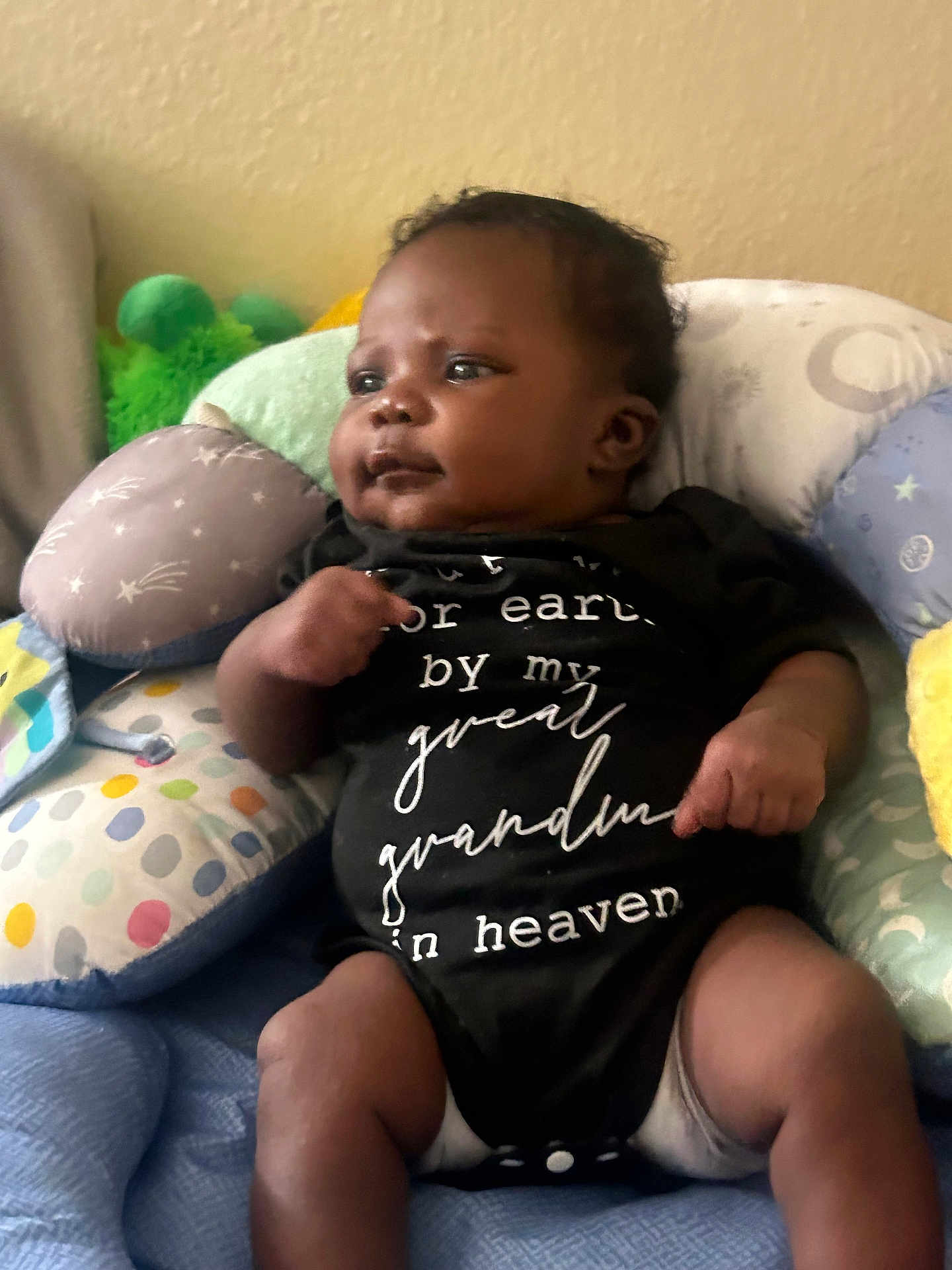 Oshun joined the competition — help win amazing prizes! baby, black_clothing, child, chubby_cheeks, colorful_pillows, comfort, curious_gaze, cute, fabric, face, hands, indoor, infant, legs, onesie, pillow, relaxed, seated, soft_lighting, wall