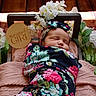 Emma joined the competition — help win amazing prizes! baby, infant, newborn, sleeping, swaddled, floral_blanket, headband, flower_arrangement, wooden_floor, pink_cushion, portrait, peaceful, cute, child, resting, soft_lighting, sign, decor, indoors, cozy