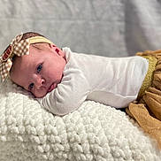 Layla joined the competition — help win amazing prizes! baby, infant, headband, bow, blanket, white, golden_skirt, clothing, soft_texture, closeup, portrait, face, person, cute, resting, indoors, soft_lighting, newborn, toddler, cozy