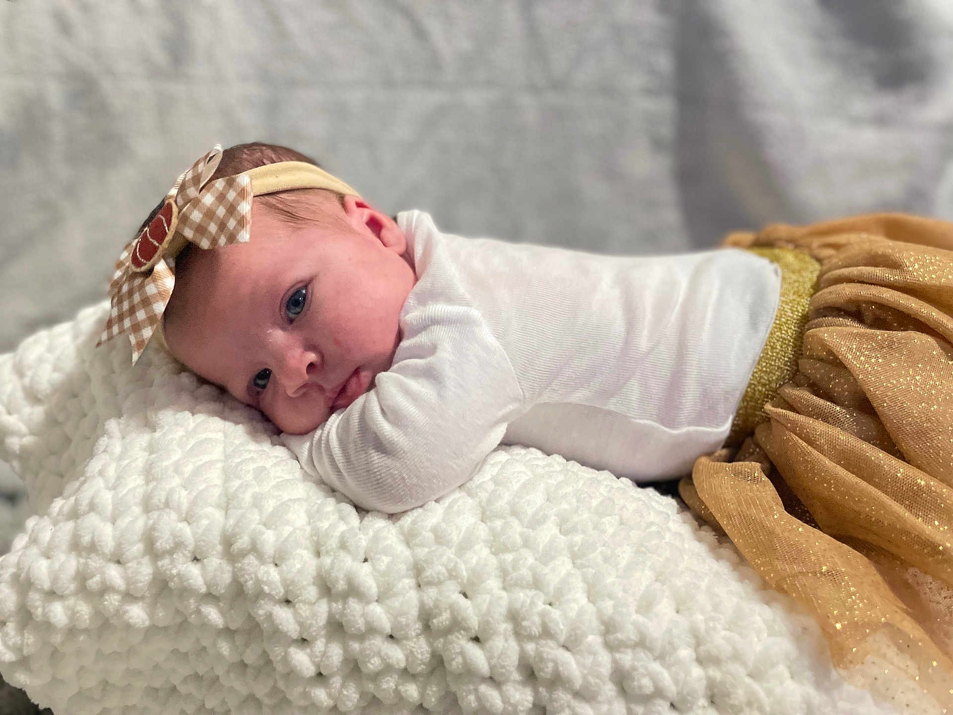 Layla joined the competition — help win amazing prizes! baby, infant, headband, bow, blanket, white, golden_skirt, clothing, soft_texture, closeup, portrait, face, person, cute, resting, indoors, soft_lighting, newborn, toddler, cozy