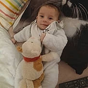 Lisandro a rejoint le concours — aidez-le/la à gagner de superbes lots ! baby, stuffed_animal, pillow, remote_control, bed, blanket, smile, infant, clothing, face, person, soft_toy, cute, indoor, resting, cozy, child, toddler, plush, animal_print