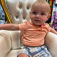 Everett joined the competition — help win amazing prizes! baby, child, toddler, chair, gold, white, plaid_shorts, peach_shirt, furniture, indoor, cute, portrait, sitting, young_child, person, face, expression, curious, comfortable, decor