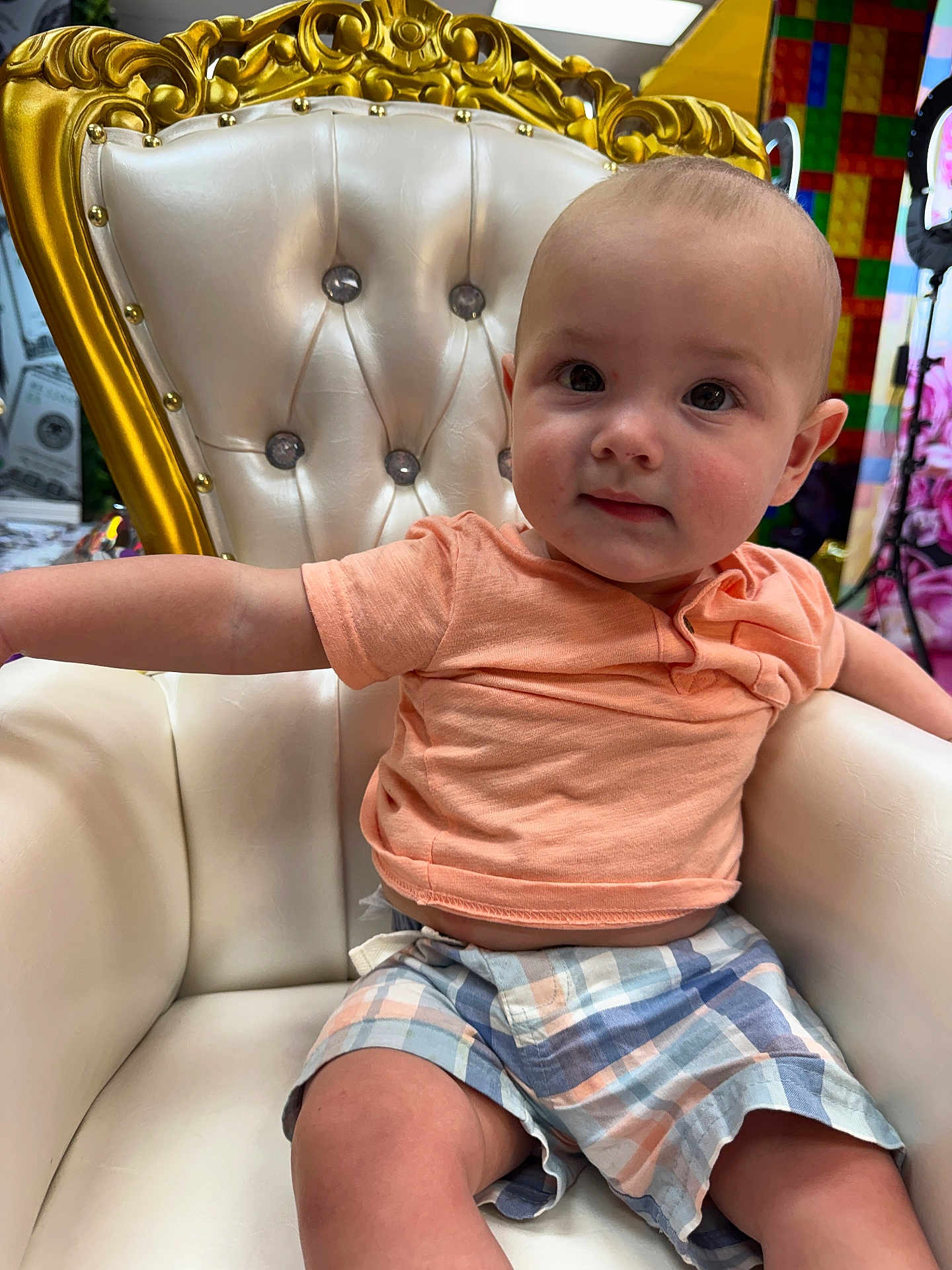 Everett joined the competition — help win amazing prizes! baby, child, toddler, chair, gold, white, plaid_shorts, peach_shirt, furniture, indoor, cute, portrait, sitting, young_child, person, face, expression, curious, comfortable, decor
