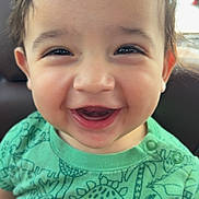Xavier is registered to the contest to win money with this photo: toddler, child, smiling, happy, green_shirt, dinosaur_pattern, face, portrait, cute, baby, person, sitting, hand, indoor, young_child, emotion, joy, casual_clothing, closeup, bright