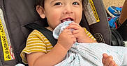 Xavier is registered to the contest to win money with this photo: toddler, child, stroller, blanket, grass, outdoor, happy, smiling, feet, clothing, person, baby, playful, curly_hair, seatbelt, yellow, striped, park, cute, chewing