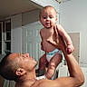 Juan is registered to the contest to win money with this photo: baby, adult, indoor, diaper, lifting, holding, shirtless, person, child, face, arm, expression, room, door, construction, skin, head, hand, male, parenting