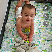 Juan is registered to the contest to win money with this photo: baby, child, playpen, toy, stuffed_animal, dinosaur_pattern, crawling, smiling, diaper, indoor, floor, cute, infant, young_child, colorful, fabric, soft_toys, happy, person, playtime