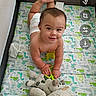 baby, child, playpen, toy, stuffed_animal, dinosaur_pattern, crawling, smiling, diaper, indoor, floor, cute, infant, young_child, colorful, fabric, soft_toys, happy, person, playtime