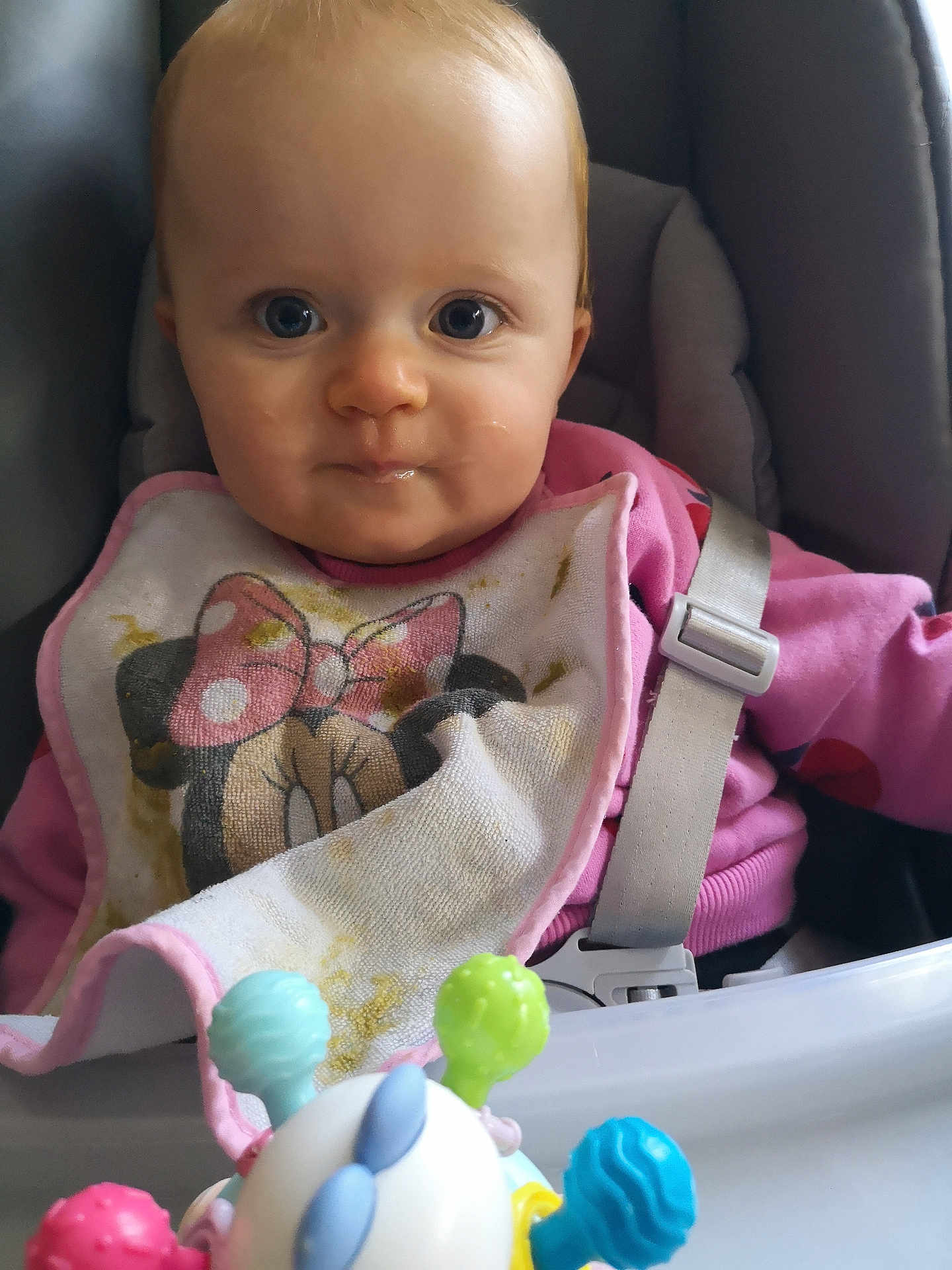 Eloane participe au concours pour gagner de l'argent avec cette photo : baby, bib, high_chair, toy, face, blue_eyes, pink_clothing, seatbelt, mickey_mouse, minnie_mouse, child, indoor, infant, cute, messy, feeding, closeup, person, playful, smiling