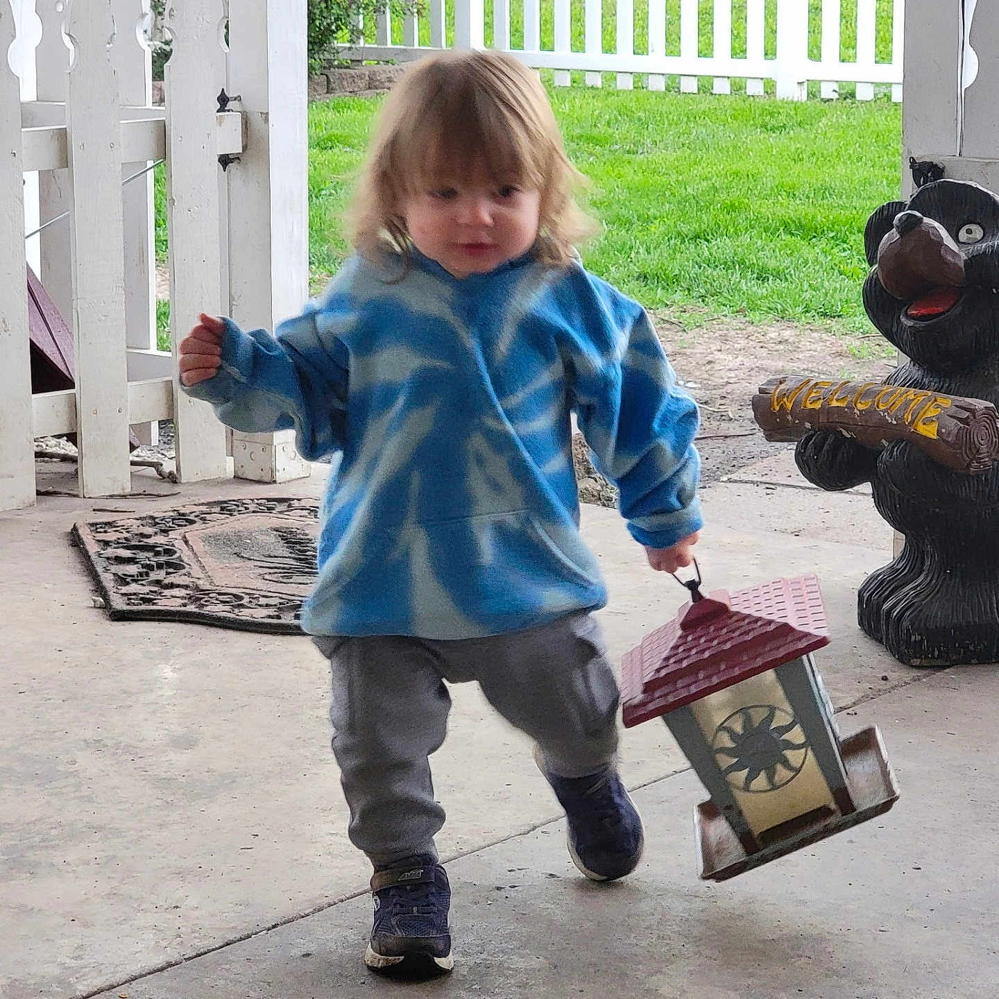 Lokie joined the competition — help win amazing prizes! bear_statue, blue_hoodie, casual_clothing, child, concrete_floor, cute, daylight, decorative_object, grass, lantern, outdoor, person, playful, porch, shoes, toddler, walking, welcome_sign, white_picket_fence, young_child