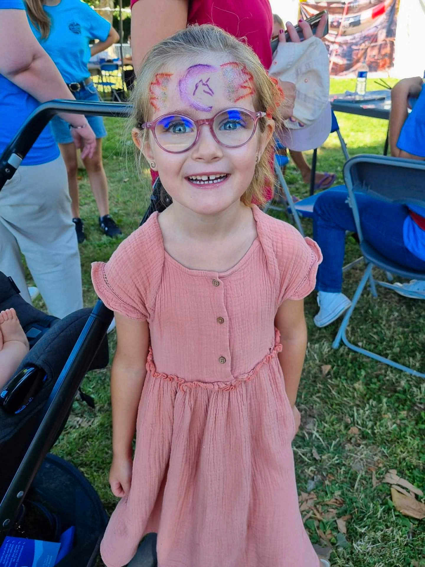 Angèle participe au concours pour gagner de l'argent avec cette photo : child, girl, face_paint, glasses, pink_dress, smiling, outdoor, grass, people, event, chair, stroller, happy, summer, sunlight, portrait, casual, festival, young, fun